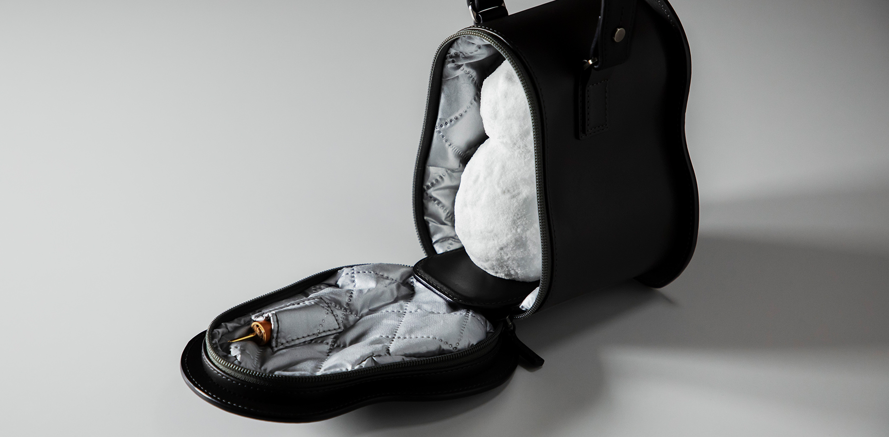 A photo of a carrier designed specifically to carry a small snowman. It is a black hard-shell cooler bag shaped like a small snowman, open with a snowman inside of it.